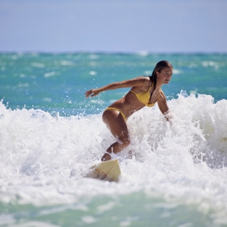 Teenage girl in a yellow bikini surfing in Hawaii